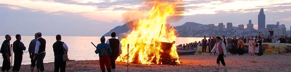 a group of people standing around a fire on a beach